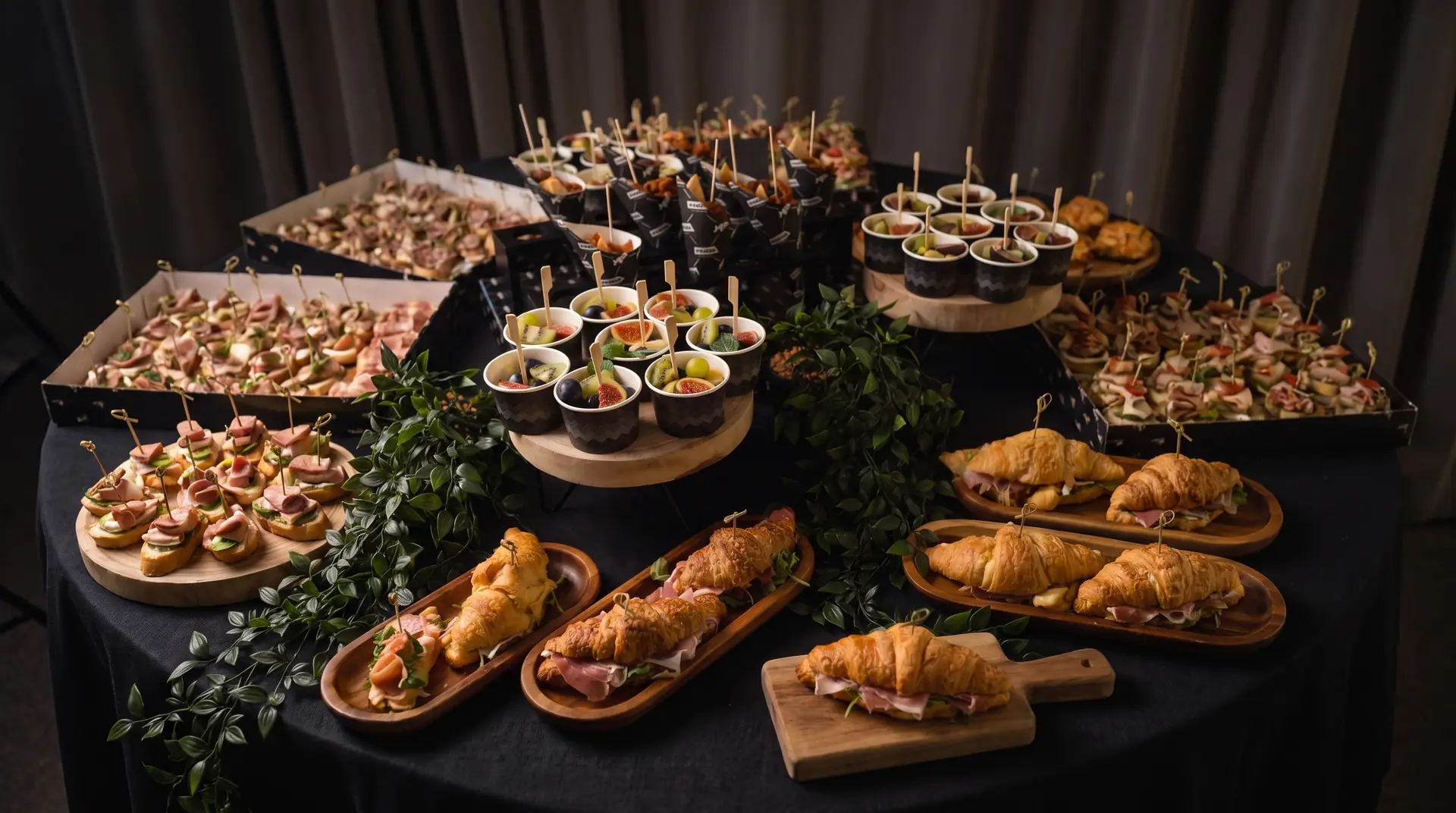 Bogato postavljena miza s finger food prigrizki, mini rogljički s pršutom in sadnimi kozarčki